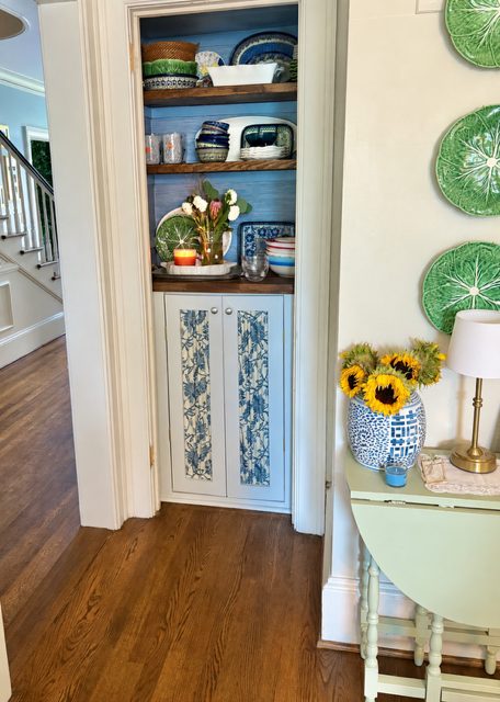 Hall nook with blue-backed shelves, chinoiserie cabinet panels, and cabbage-leaf plates