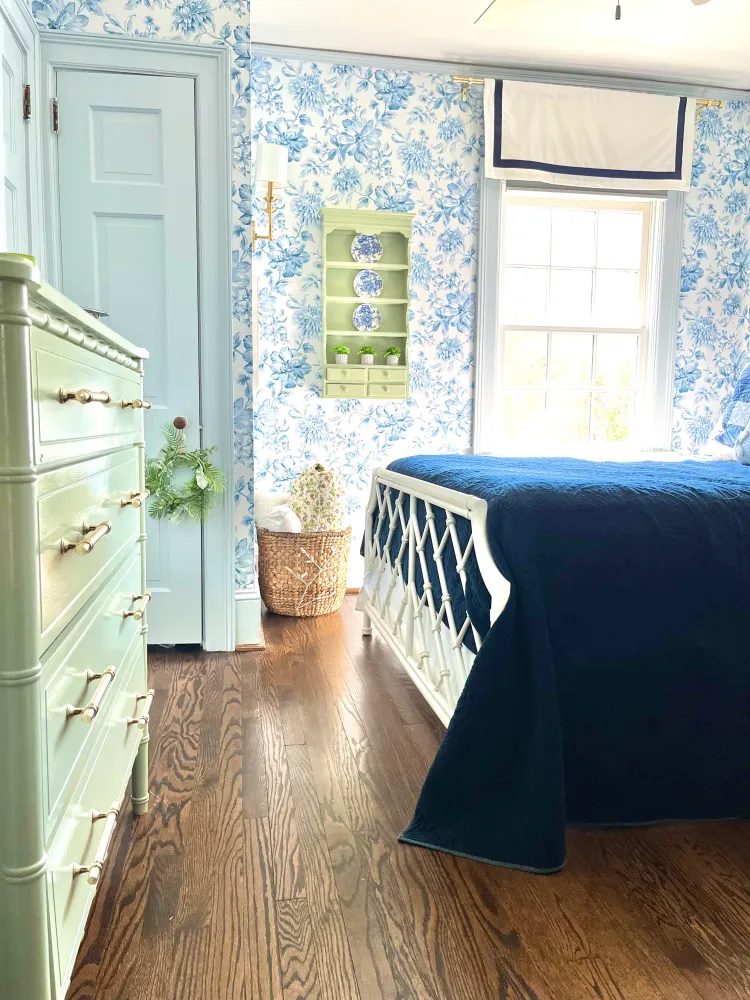 Guest bedroom with blue-and-white floral wallpaper, a celadon bamboo dresser, and a navy quilt