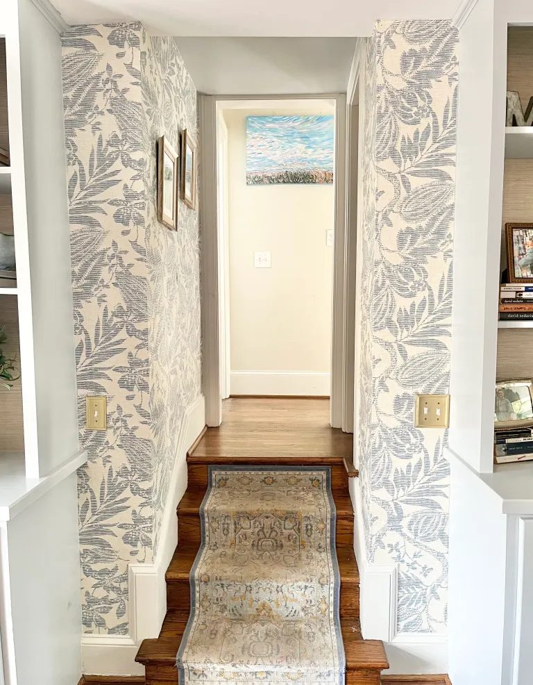 Short stair hall wrapped in blue botanical wallpaper with a patterned runner