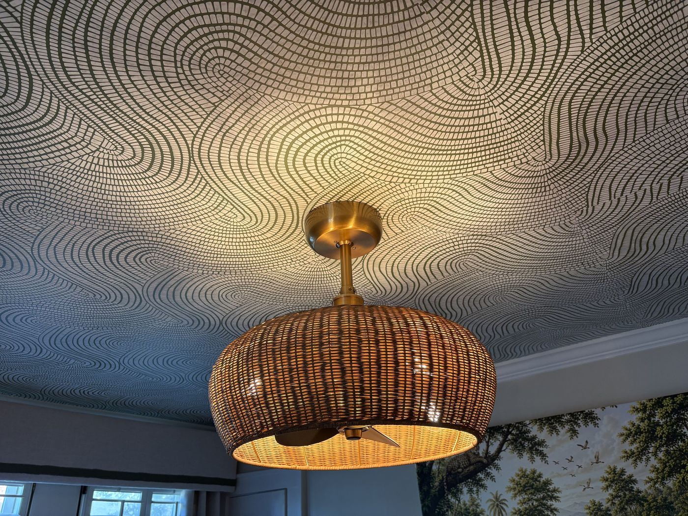 Rattan pendant light against a swirl-patterned wallpapered ceiling