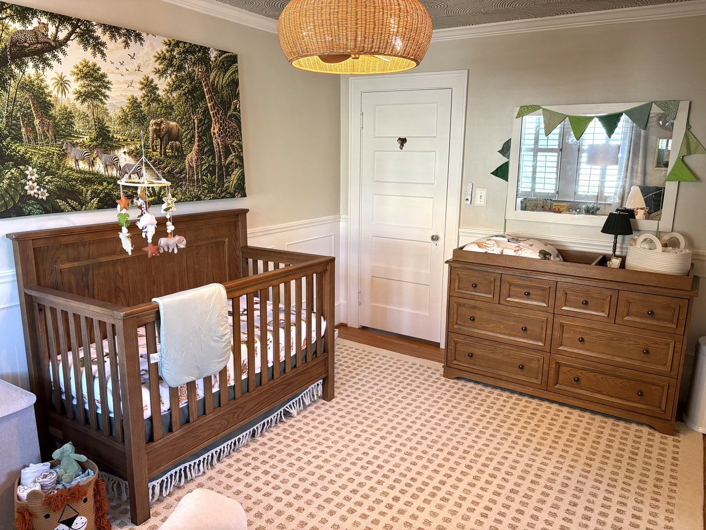 Nursery with a wood crib, safari mural, rattan pendant, and patterned rug
