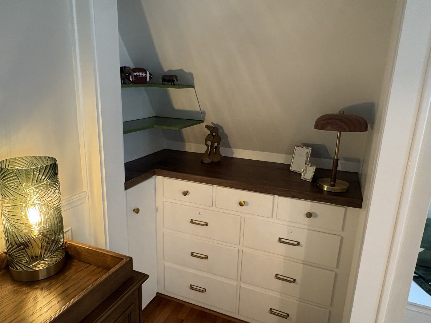 Built-in desk nook with white drawers, a walnut top, and green floating shelves