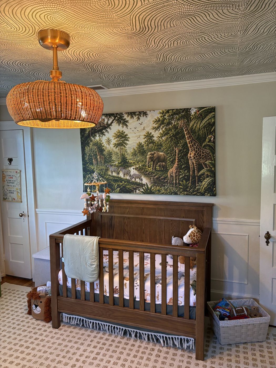 Nursery with a wood crib beneath a safari mural, rattan pendant, and swirl-patterned ceiling