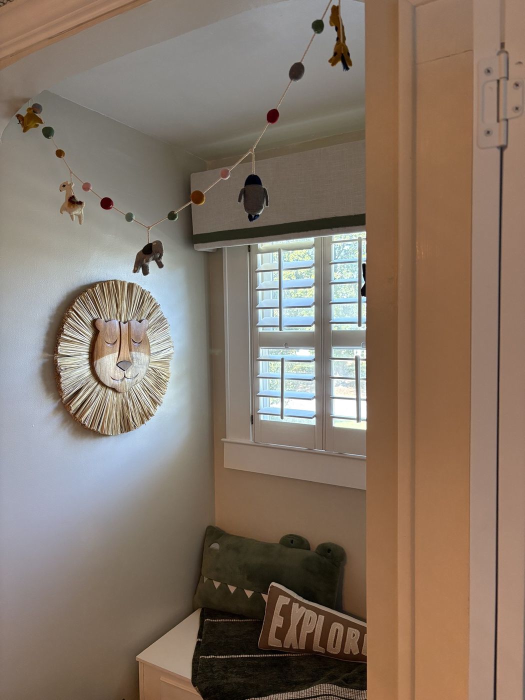 Nursery window nook with a woven lion head, animal garland, and storage bench