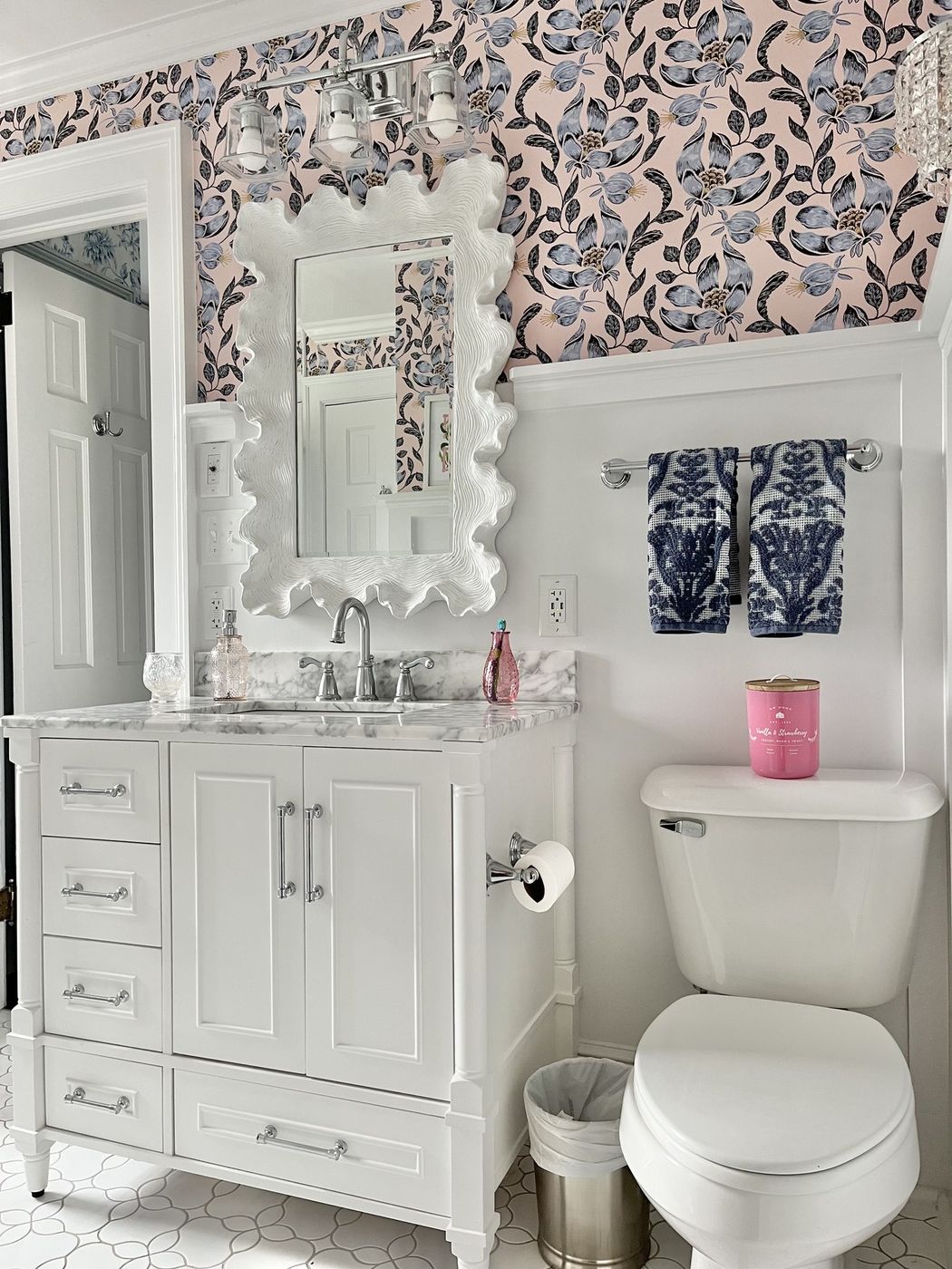 Powder room with pink floral wallpaper, a white scalloped mirror, and a marble-top vanity