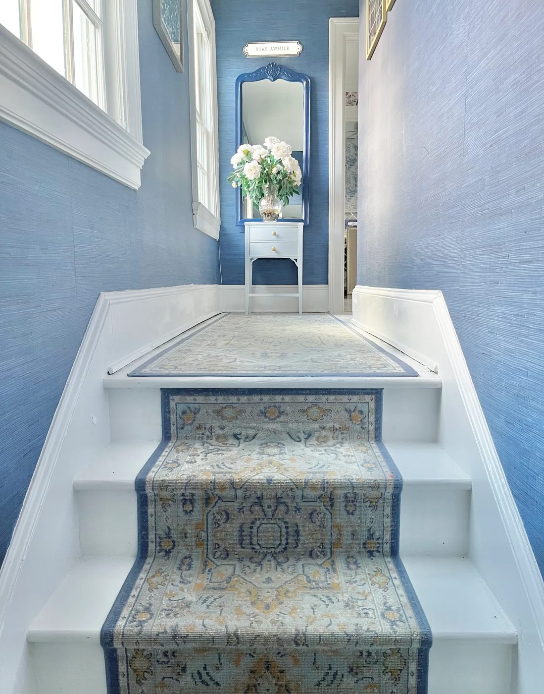 Stair landing with blue grasscloth walls, a lacquered blue mirror, and a patterned runner